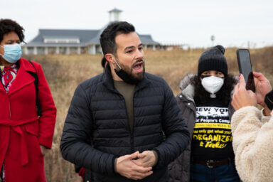 Jonathan Soto speaks with his hands together, looking off camera while speaking outside the Trump Links at Ferry Point Park site.