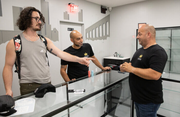 Matt Catalano points to a product in Levent Ozkurt's hand while Denis Ozkurt smiles