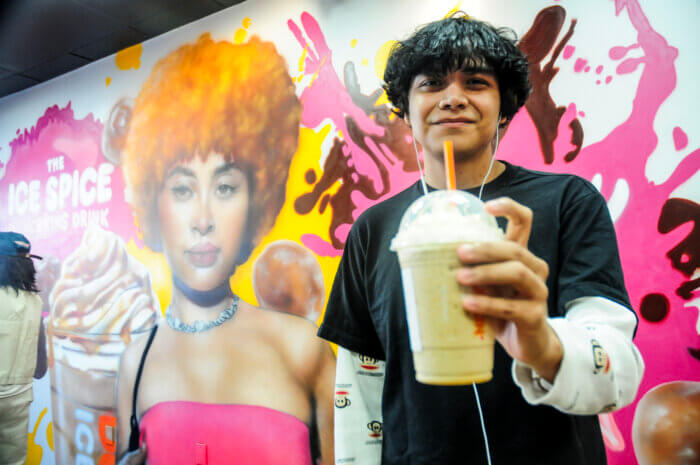 The Ice Spice Munchkins Drink, according to Dunkin' Donuts, blends the establishment's signature frozen coffee with Pumpkin MUNCHKINS Donut Hole Treats, and is topped with whipped cream and caramel drizzle. Pictured here, Fordham Heights resident George Ortega, 21, attends the mural unveiling and tries the new signature drink.