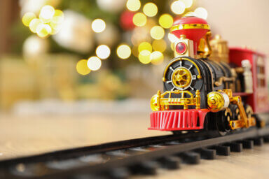 Toy train and railway on floor against Christmas lights. Space for text