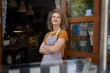 Caucasian waitress standing in apron outside of cafe and looking around