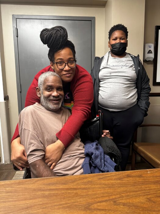 Cheree Evans hugs her uncle, Frederick "Freddy" Simmons in the Williamsbridge Center nursing facility after reuniting with him in November 2023. Her son, Jared Catlin, stands to the right. Bronx, NY.