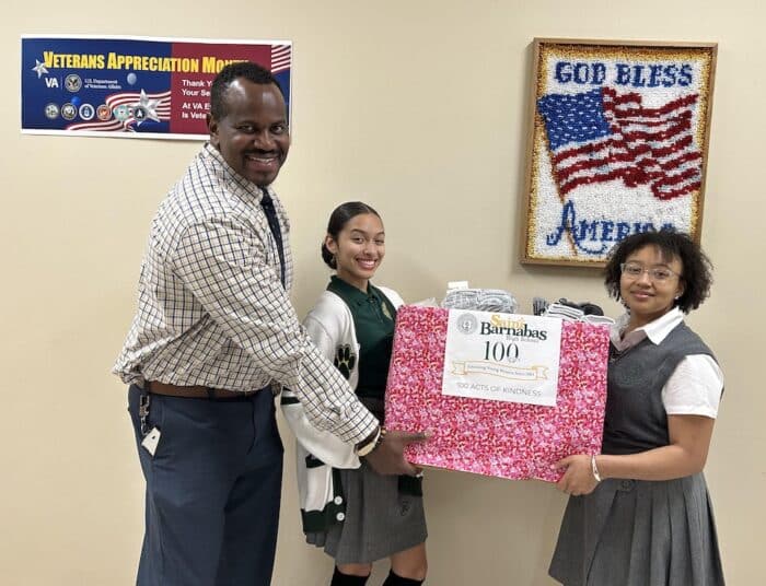 Two student representatives from Saint Barnabas High School hold a box of socks to donate to veterans.