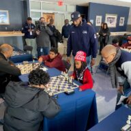 Project Pawn founder Abdul Sulaiman Jr. (center) and New York City Schools Chancellor David Banks (right) watch students play chess at Yankee Stadium.
