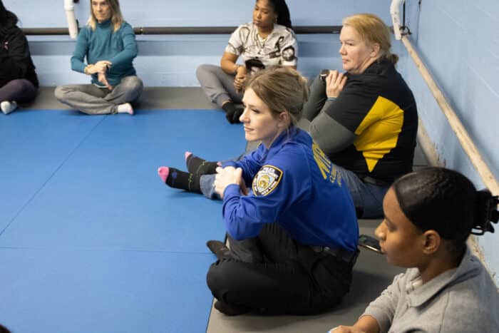 Officer Rivera and workshop attendees stretch with instructor Luiz Gustavo Costa before the women's self defense class.
