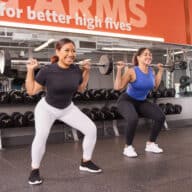 Two women lift weights at a Blink Fitness gym.