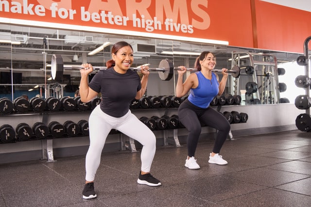Two women lift weights at a Blink Fitness gym.