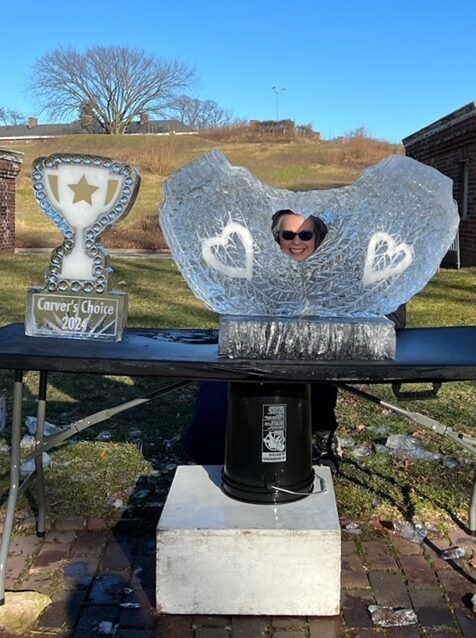 Lovie Pignata smiles through the heart-shaped hole in her sculpture, formed by the mittens. Beside her is the Carver's Choice trophy, made from ice.