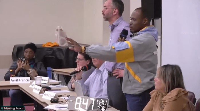 CB11 District Manager Jeremy Warneke, left, and board member Malcom Gray, right with the microphone, try to settle a full meeting on Thursday, April 25, 2024.