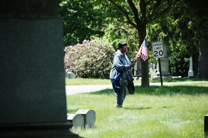 A Community Board Seven member walks the grass of Woodlawn Cemetery in northern Bronx holding an American flag on May 20, 2024.