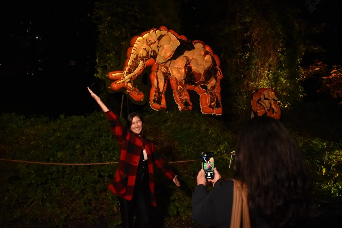 a woman poses in front of a pumpkin carving of an elephant at the bronx zoo
