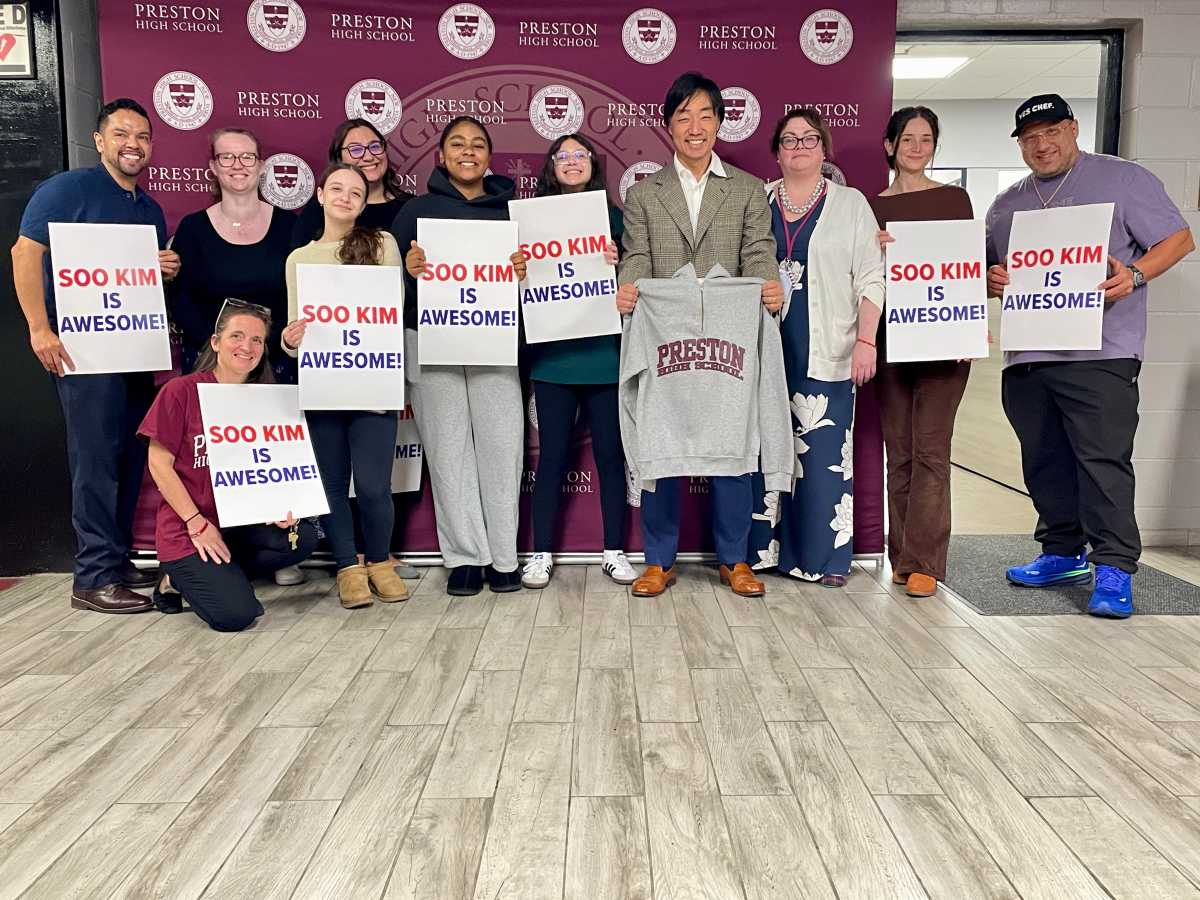 Bally's Chair Soo Kim proudly displays his very own Preston High School hoodie while grateful students parents and school administrators show off signs that read "Soo Kim is Awesome."