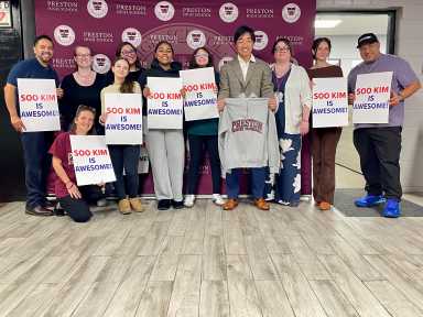 Bally's Chair Soo Kim proudly displays his very own Preston High School hoodie while grateful students parents and school administrators show off signs that read "Soo Kim is Awesome."