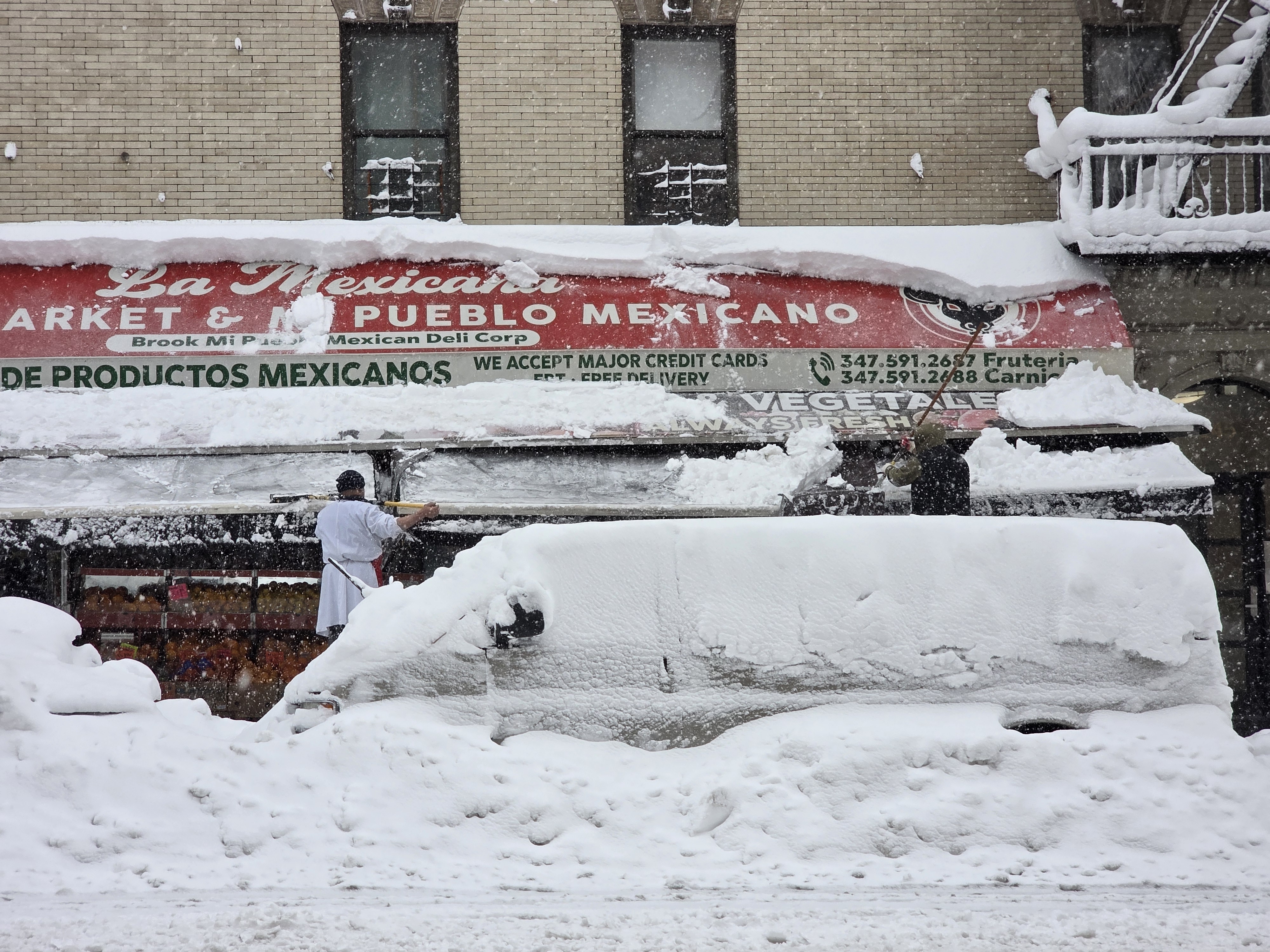 Workers clear snow from the awning at Mi Pueblo Mexican Deli at East 138th St. and Brook Ave.