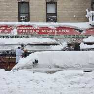 Workers clear snow from the awning at Mi Pueblo Mexican Deli at East 138th St. and Brook Ave.
