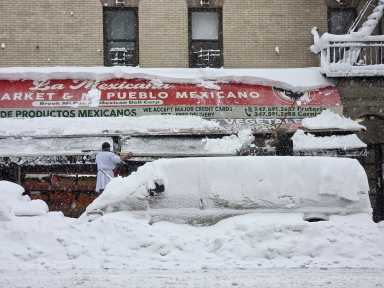 Workers clear snow from the awning at Mi Pueblo Mexican Deli at East 138th St. and Brook Ave.