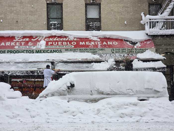 Workers clear snow from the awning at Mi Pueblo Mexican Deli at East 138th St. and Brook Ave.
