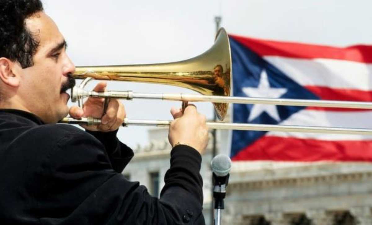 Willie Colon playing his trombone in front of a Puerto Rican flag.