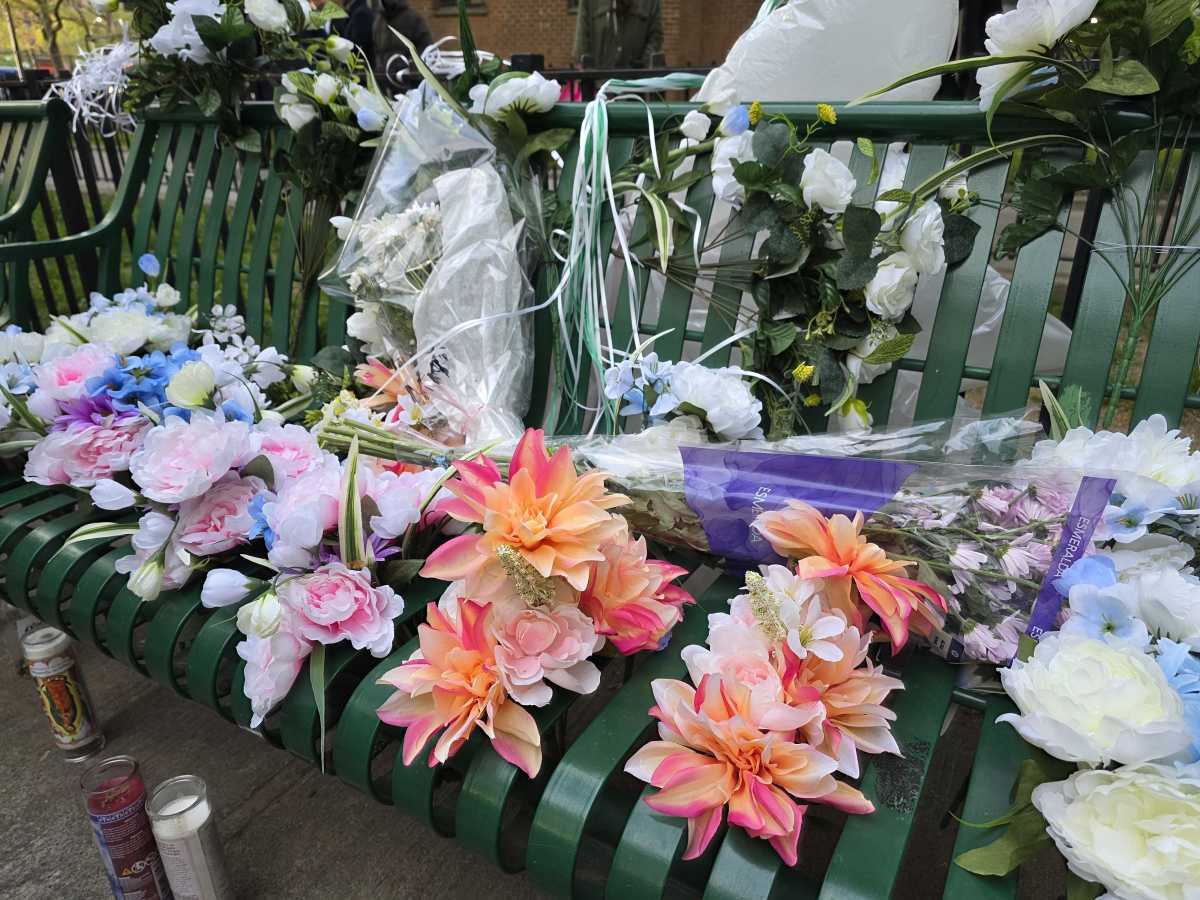 Flowers, garlands, and candles lay on the bench where 78-year old Edgar Spence was killed by a stray bullet on Thursday.