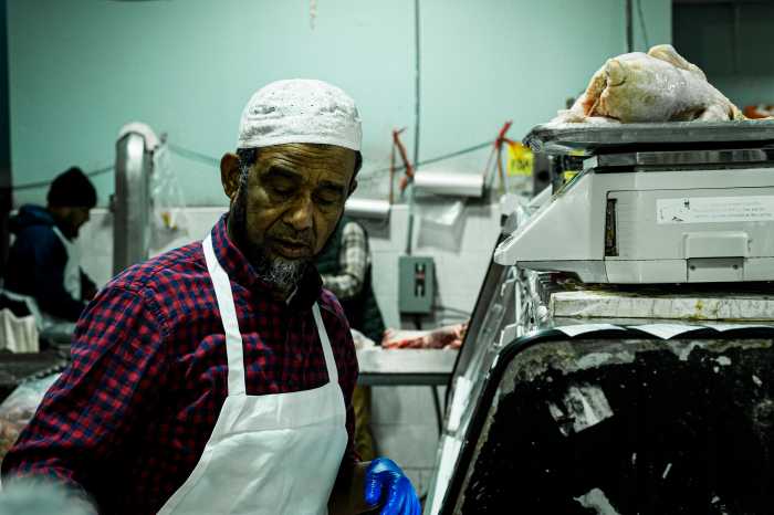 A butcher weighs a chicken at the halal meat counter at Al-Aqsa Supermarket in Bangla Bazaar.