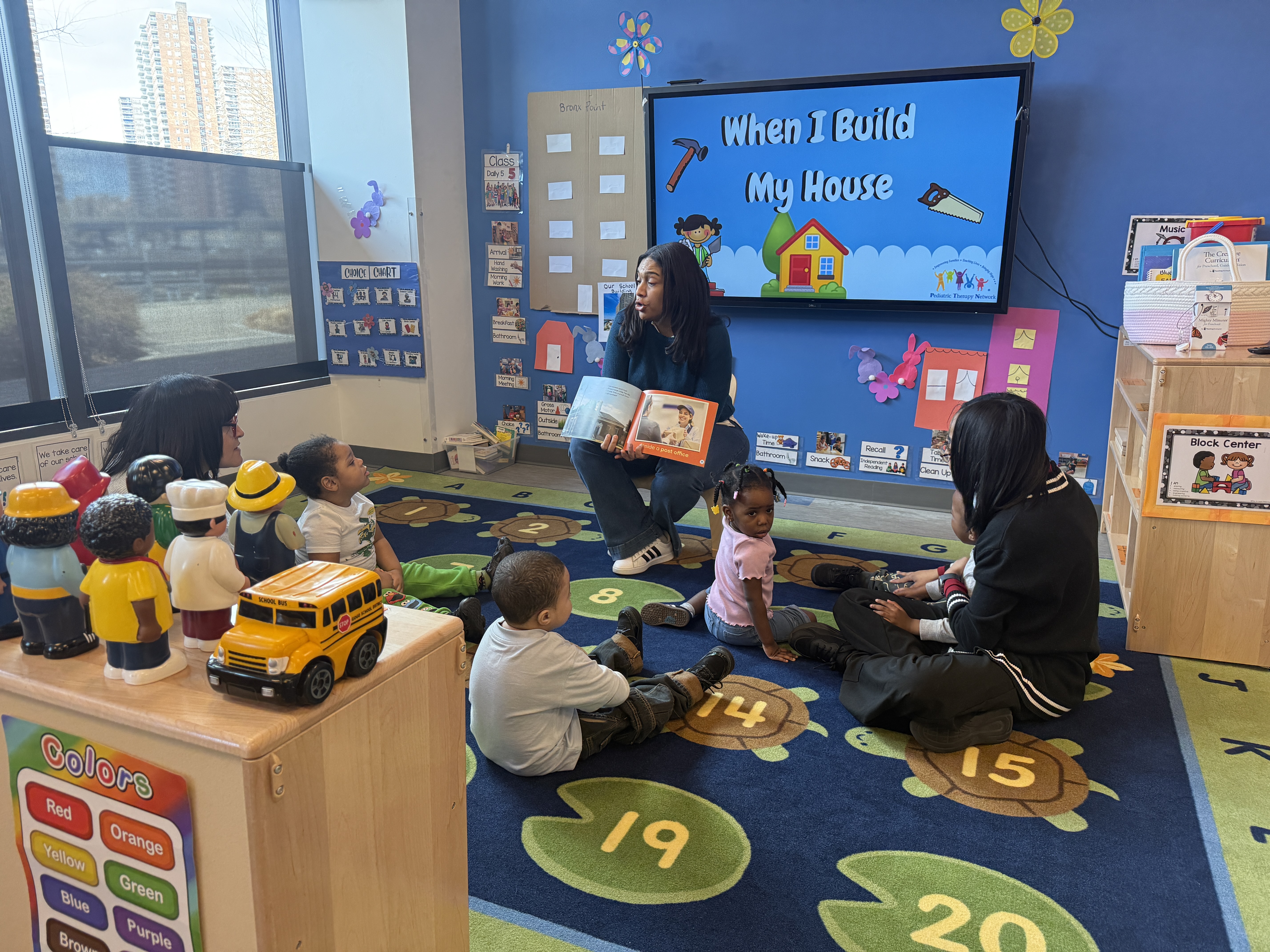 Three teachers at BronxWorks leading story time for a mixed-age group of children.