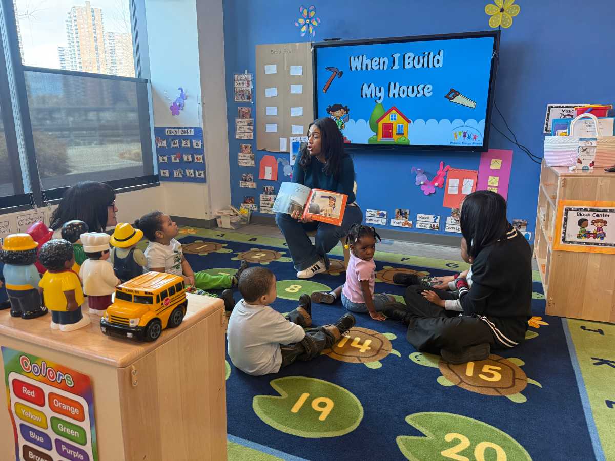 Three teachers at BronxWorks leading story time for a mixed-age group of children.