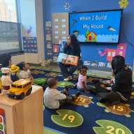Three teachers at BronxWorks leading story time for a mixed-age group of children.