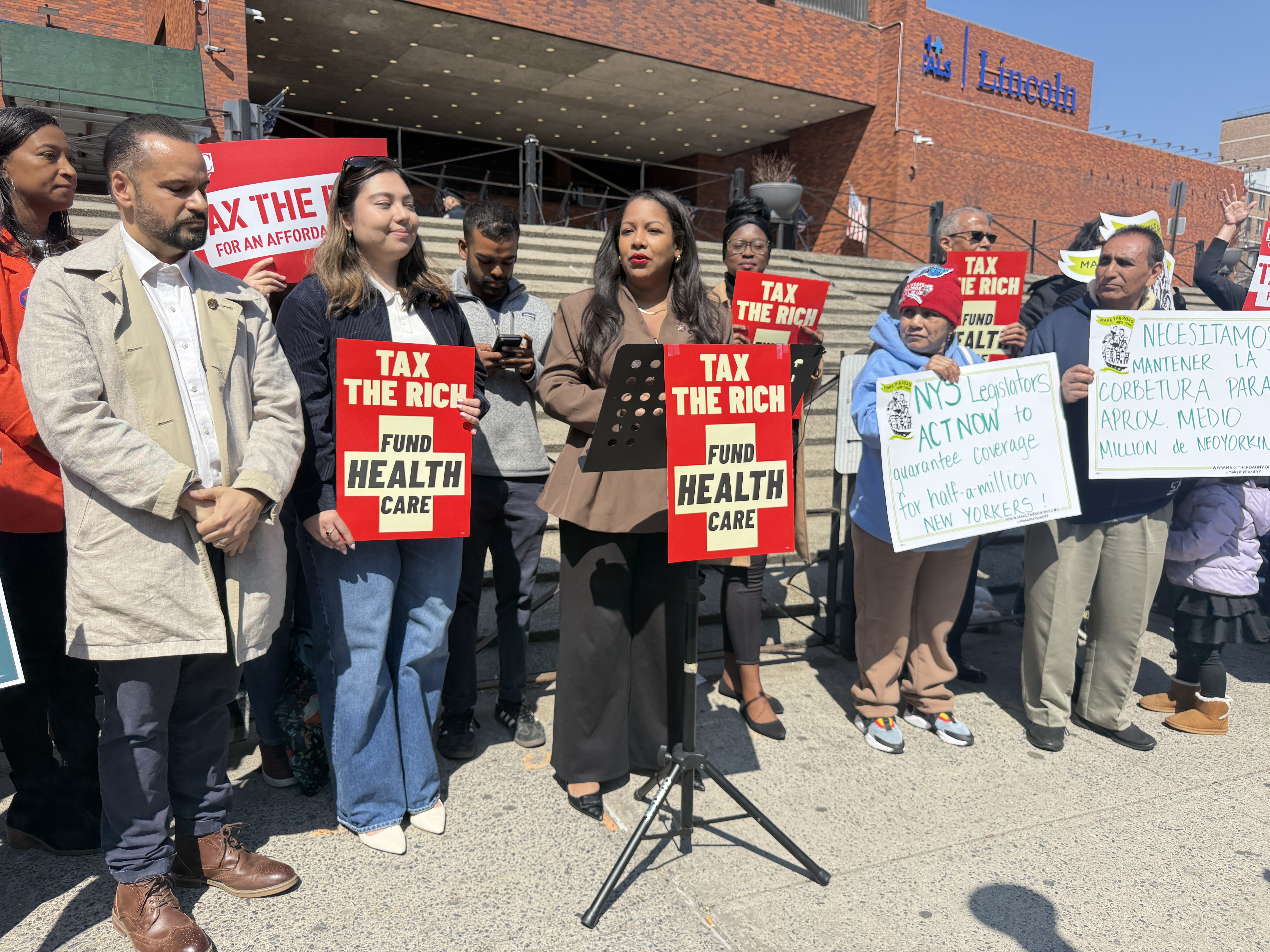 Assemblymember Amanda Septimo speaks out against the Essential Plan cuts at the Tax the Rich rally, alongside State Sens. Jose Serrano and Kristen Gonzalez.